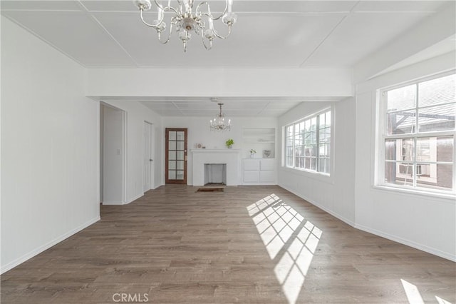 unfurnished living room featuring wood-type flooring, a healthy amount of sunlight, and a notable chandelier