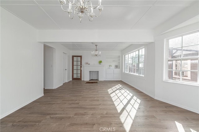 unfurnished living room with an inviting chandelier, a fireplace, built in features, and wood finished floors