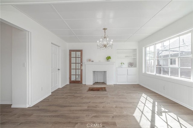 unfurnished living room featuring hardwood / wood-style floors, a notable chandelier, built in features, and a fireplace