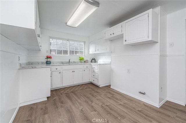 kitchen with light wood-style flooring, white cabinetry, light countertops, and a sink