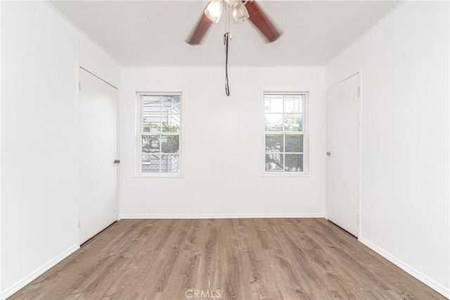 empty room featuring a healthy amount of sunlight, baseboards, ceiling fan, and wood finished floors