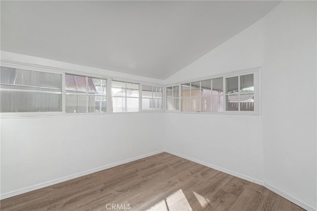 spare room with baseboards, vaulted ceiling, and wood finished floors