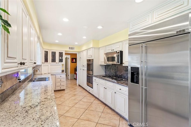 kitchen featuring backsplash, sink, light stone countertops, appliances with stainless steel finishes, and white cabinetry