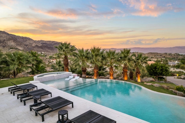 pool at dusk featuring an in ground hot tub, a mountain view, and a patio