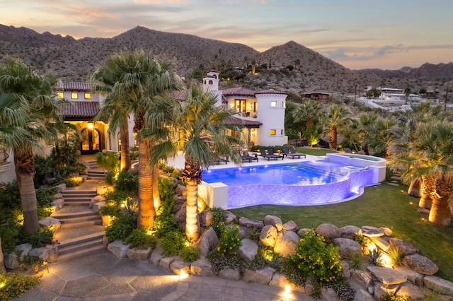 pool at dusk featuring a mountain view, a yard, and a patio