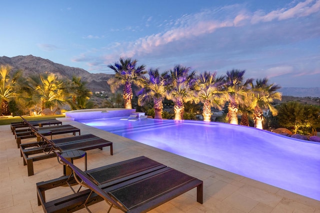 pool at dusk featuring a mountain view and a patio area