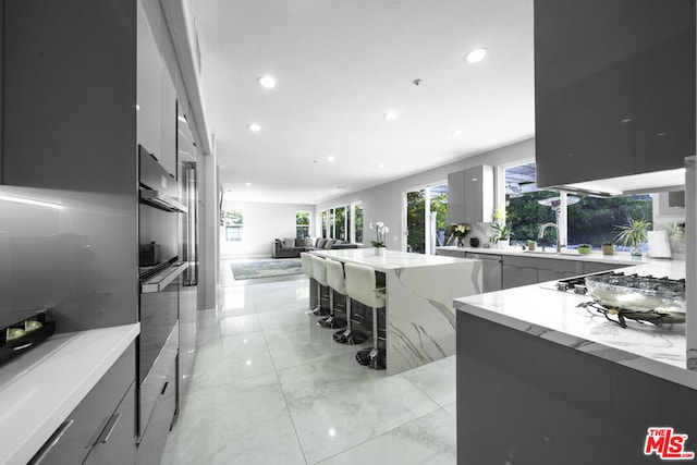 kitchen with light stone countertops, a kitchen breakfast bar, gas cooktop, and sink