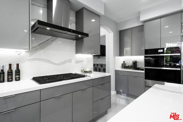 kitchen with appliances with stainless steel finishes, tasteful backsplash, wall chimney exhaust hood, and gray cabinetry