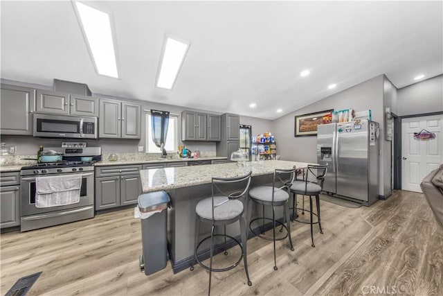 kitchen featuring a kitchen breakfast bar, stainless steel appliances, gray cabinets, a kitchen island, and lofted ceiling