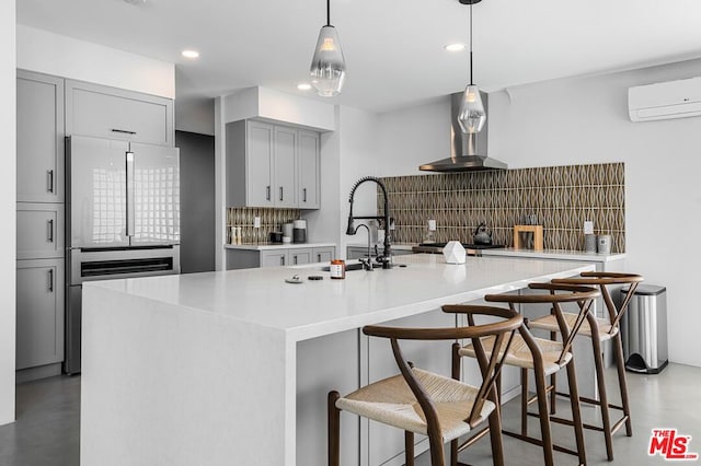 kitchen with wall chimney exhaust hood, backsplash, a wall unit AC, an island with sink, and high quality fridge