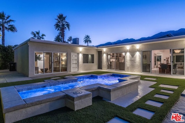 pool at dusk with an in ground hot tub and a patio