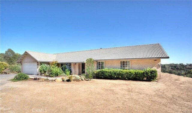 ranch-style house featuring a garage, driveway, a tile roof, and stucco siding