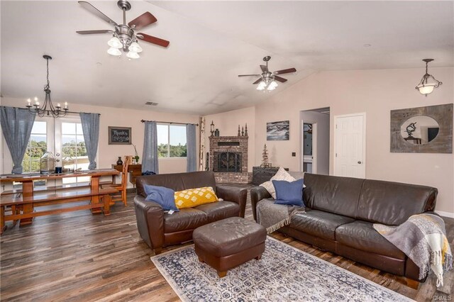 living room with wood-type flooring, ceiling fan with notable chandelier, a brick fireplace, and vaulted ceiling