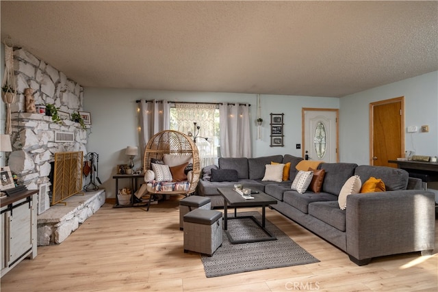 living room featuring a stone fireplace, a textured ceiling, and light hardwood / wood-style flooring