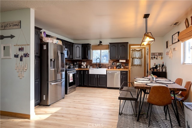 kitchen featuring sink, light hardwood / wood-style flooring, backsplash, appliances with stainless steel finishes, and decorative light fixtures