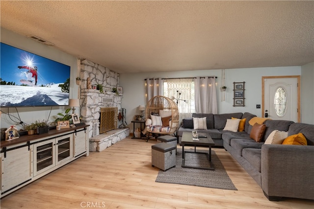 living room featuring a stone fireplace, a textured ceiling, light hardwood / wood-style flooring, and plenty of natural light