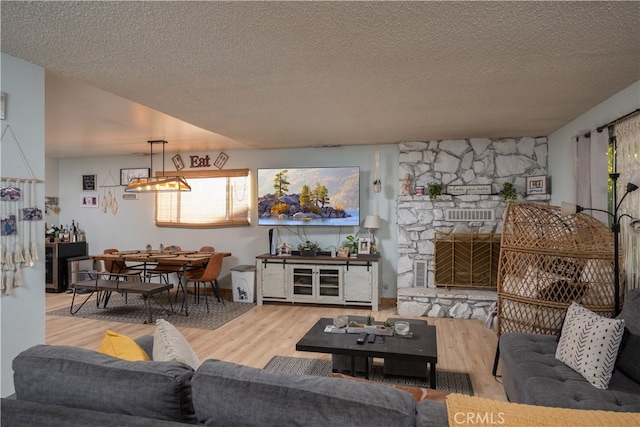 living room featuring a textured ceiling, a stone fireplace, and hardwood / wood-style floors