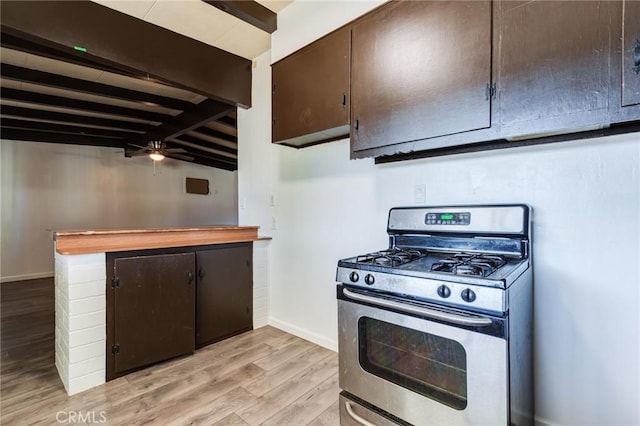 kitchen with stainless steel gas range oven, light hardwood / wood-style flooring, ceiling fan, beamed ceiling, and dark brown cabinets