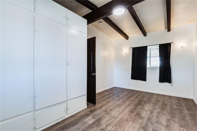 unfurnished bedroom with vaulted ceiling with beams and light wood-type flooring