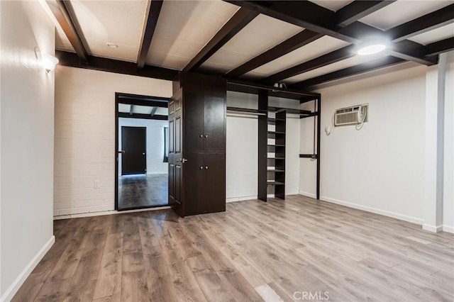 spare room with beam ceiling, light hardwood / wood-style flooring, and an AC wall unit