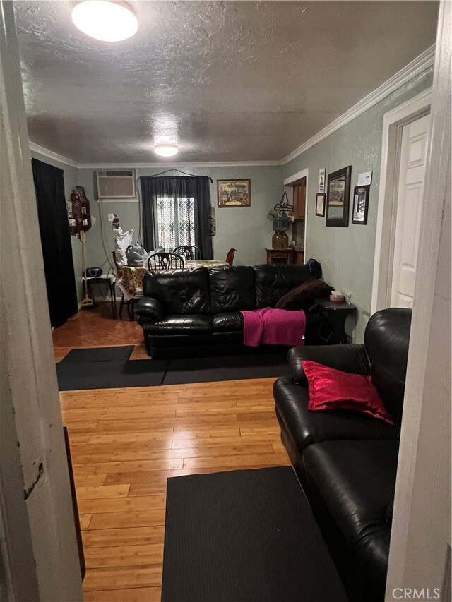 living room with a textured ceiling, crown molding, a wall mounted AC, and hardwood / wood-style flooring