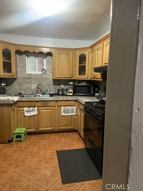 kitchen featuring decorative backsplash, black appliances, exhaust hood, and sink