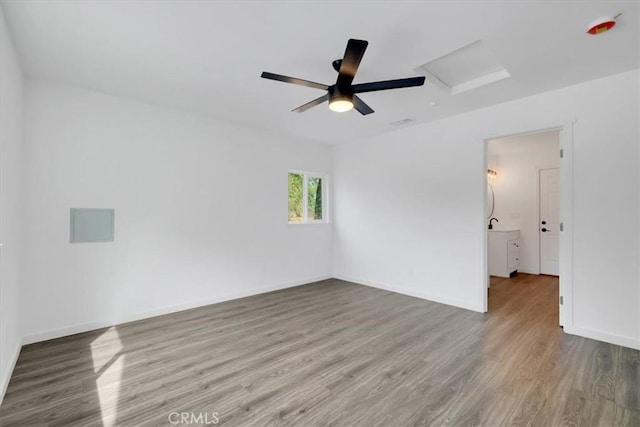 empty room with ceiling fan, wood finished floors, attic access, and baseboards