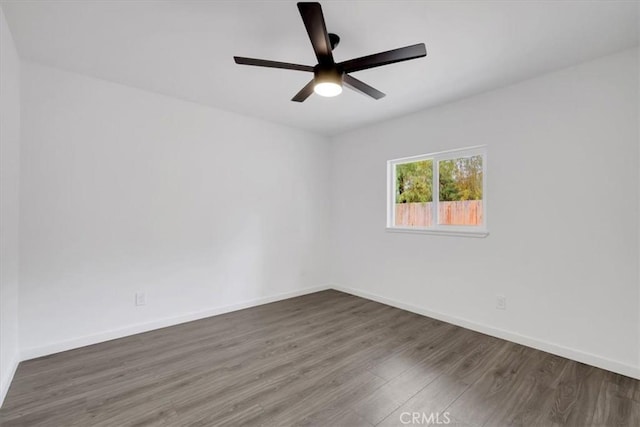 empty room with a ceiling fan, baseboards, and dark wood-type flooring