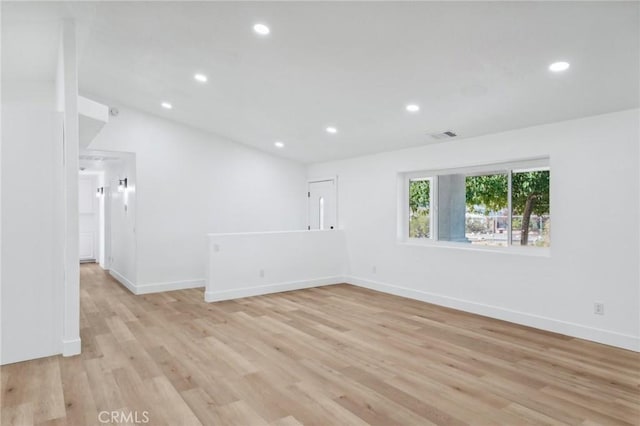 spare room featuring light wood-type flooring and vaulted ceiling