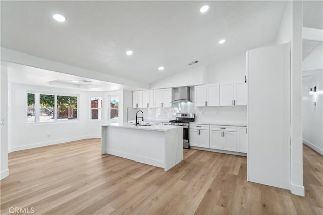 kitchen featuring tasteful backsplash, a kitchen island with sink, white cabinets, stainless steel range with gas stovetop, and wall chimney exhaust hood