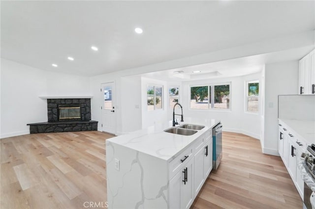 kitchen with sink, white cabinets, light stone counters, a kitchen island with sink, and stainless steel appliances