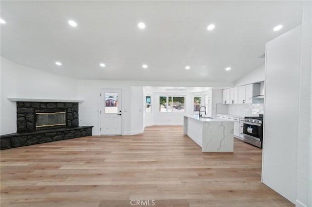 kitchen featuring wall chimney exhaust hood, white cabinetry, a stone fireplace, gas range, and light stone counters