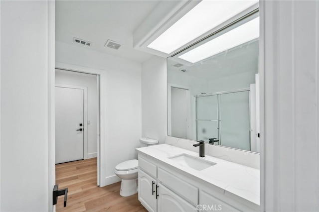 bathroom with an enclosed shower, vanity, a skylight, toilet, and hardwood / wood-style flooring