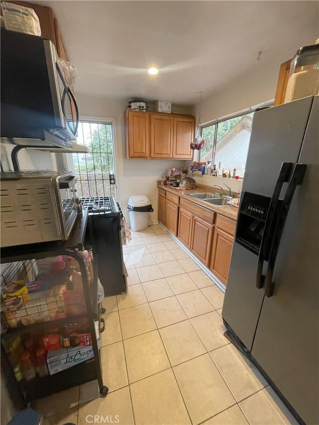 kitchen with stainless steel appliances, a wealth of natural light, light tile patterned floors, and sink