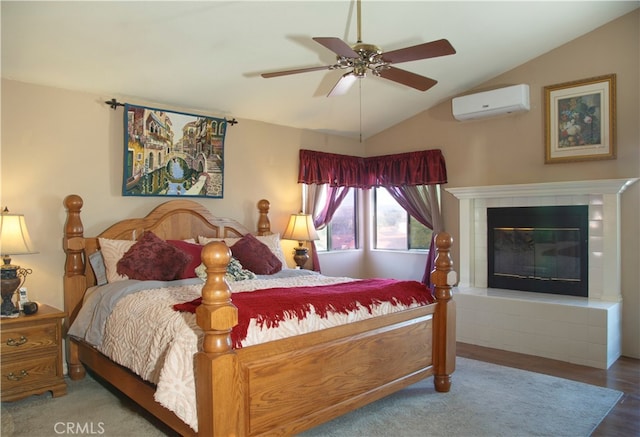 bedroom with hardwood / wood-style floors, a wall mounted AC, ceiling fan, vaulted ceiling, and a tile fireplace