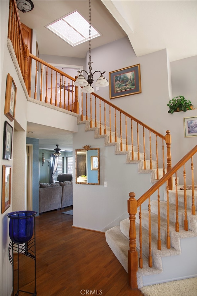 stairs with a chandelier, wood-type flooring, a high ceiling, and a skylight