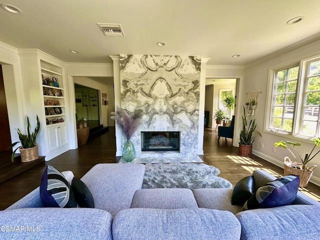 living room with built in shelves, dark hardwood / wood-style flooring, ornamental molding, and a premium fireplace