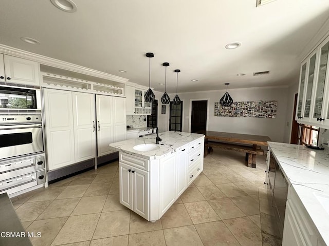 kitchen featuring white cabinets, a center island, decorative light fixtures, oven, and light stone counters