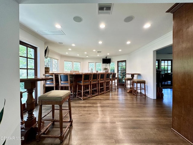 bar with dark wood-type flooring, a wealth of natural light, and ornamental molding