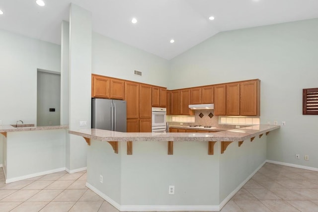 kitchen featuring stainless steel refrigerator, high vaulted ceiling, kitchen peninsula, a kitchen bar, and light tile patterned flooring