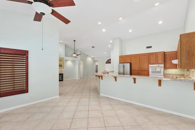 kitchen with high vaulted ceiling, oven, stainless steel fridge, kitchen peninsula, and a breakfast bar area