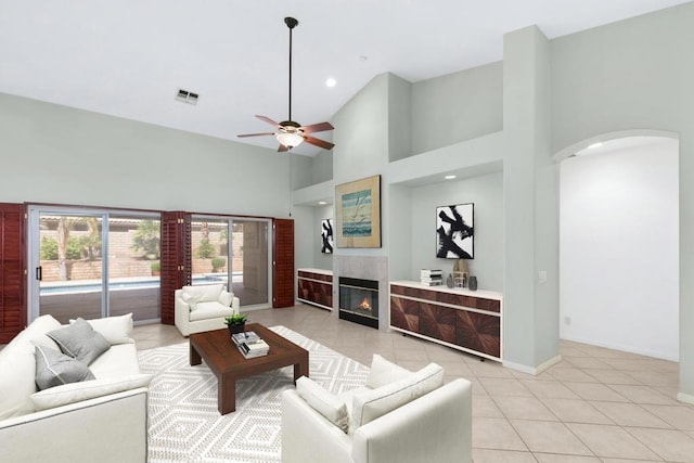 living room with a tile fireplace, a high ceiling, light tile patterned floors, and ceiling fan