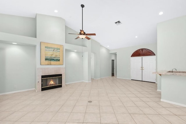 unfurnished living room with ceiling fan, sink, light tile patterned floors, high vaulted ceiling, and a fireplace