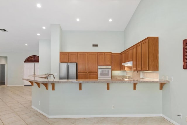 kitchen featuring stainless steel fridge, a towering ceiling, oven, and a kitchen breakfast bar