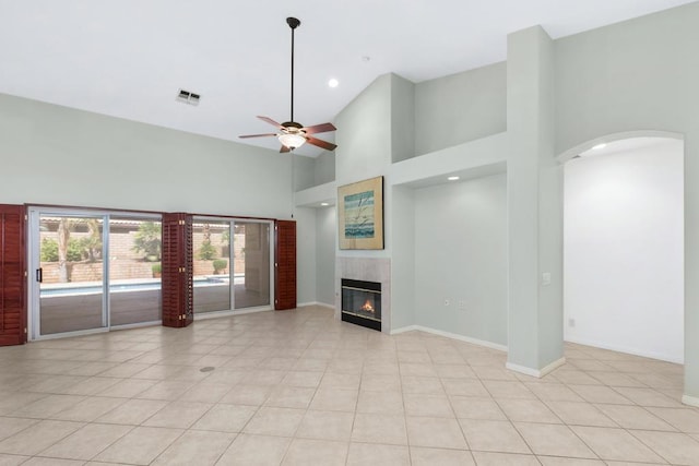 unfurnished living room with a tile fireplace, light tile patterned floors, a towering ceiling, and ceiling fan