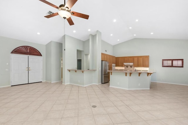 kitchen with ceiling fan, high vaulted ceiling, stainless steel fridge, a breakfast bar, and light tile patterned floors