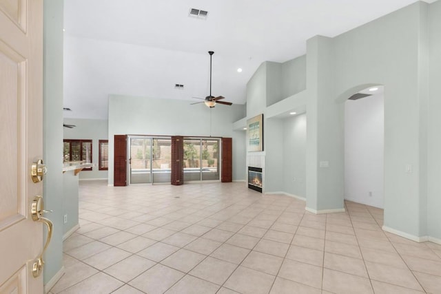 unfurnished living room with a tile fireplace, ceiling fan, high vaulted ceiling, and light tile patterned floors