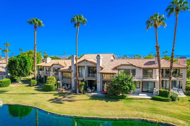 rear view of property featuring a lawn, a balcony, and a patio