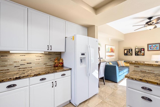 kitchen featuring white refrigerator with ice dispenser, white cabinets, tasteful backsplash, and dark stone countertops