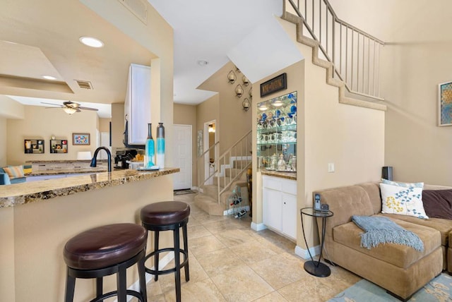 kitchen with a kitchen bar, white cabinets, ceiling fan, light tile patterned flooring, and light stone counters